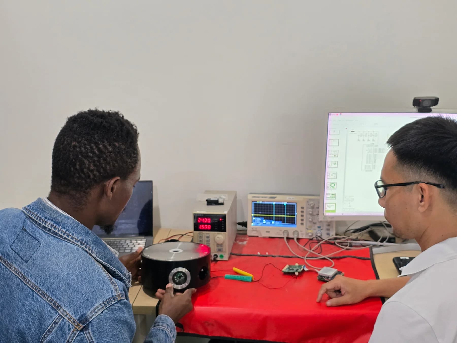 Two colleagues examining an instrument beside an oscilloscope, power supply and electronic components