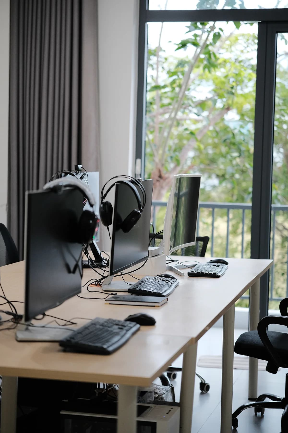 Unoccupied workstations with monitors and headsets beside a bright office window