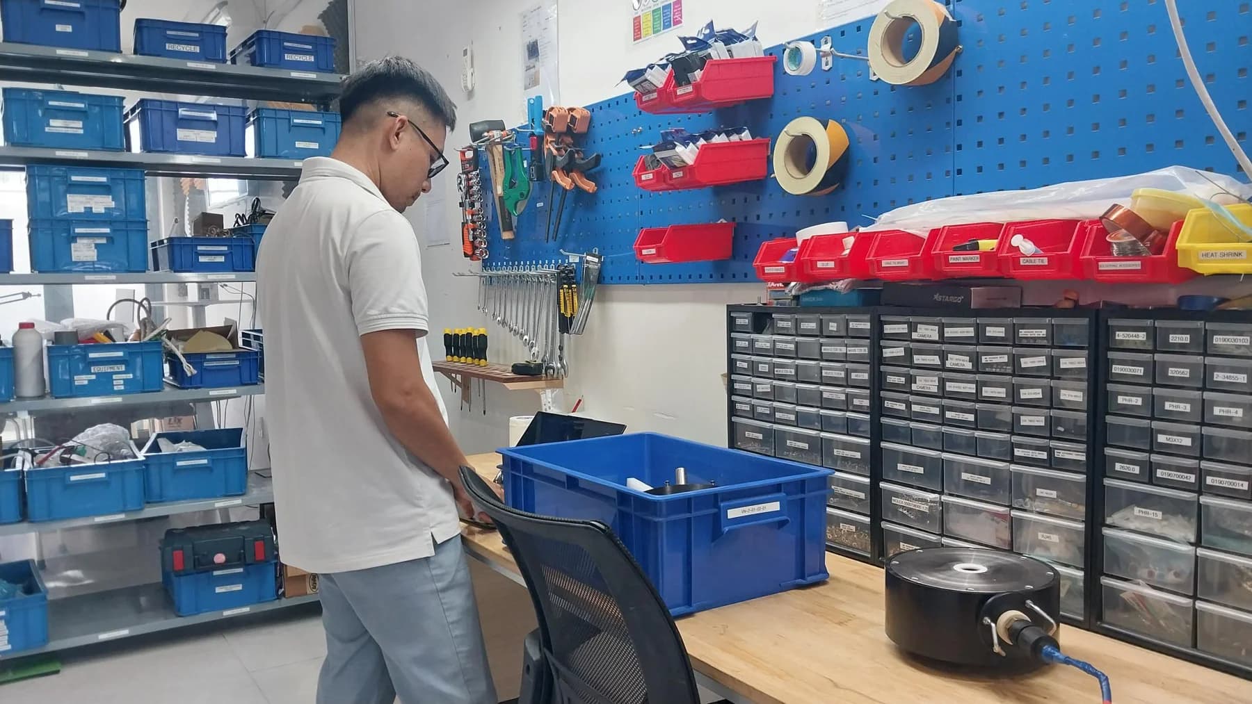A colleague at a workshop bench with tools, component drawers and an instrument