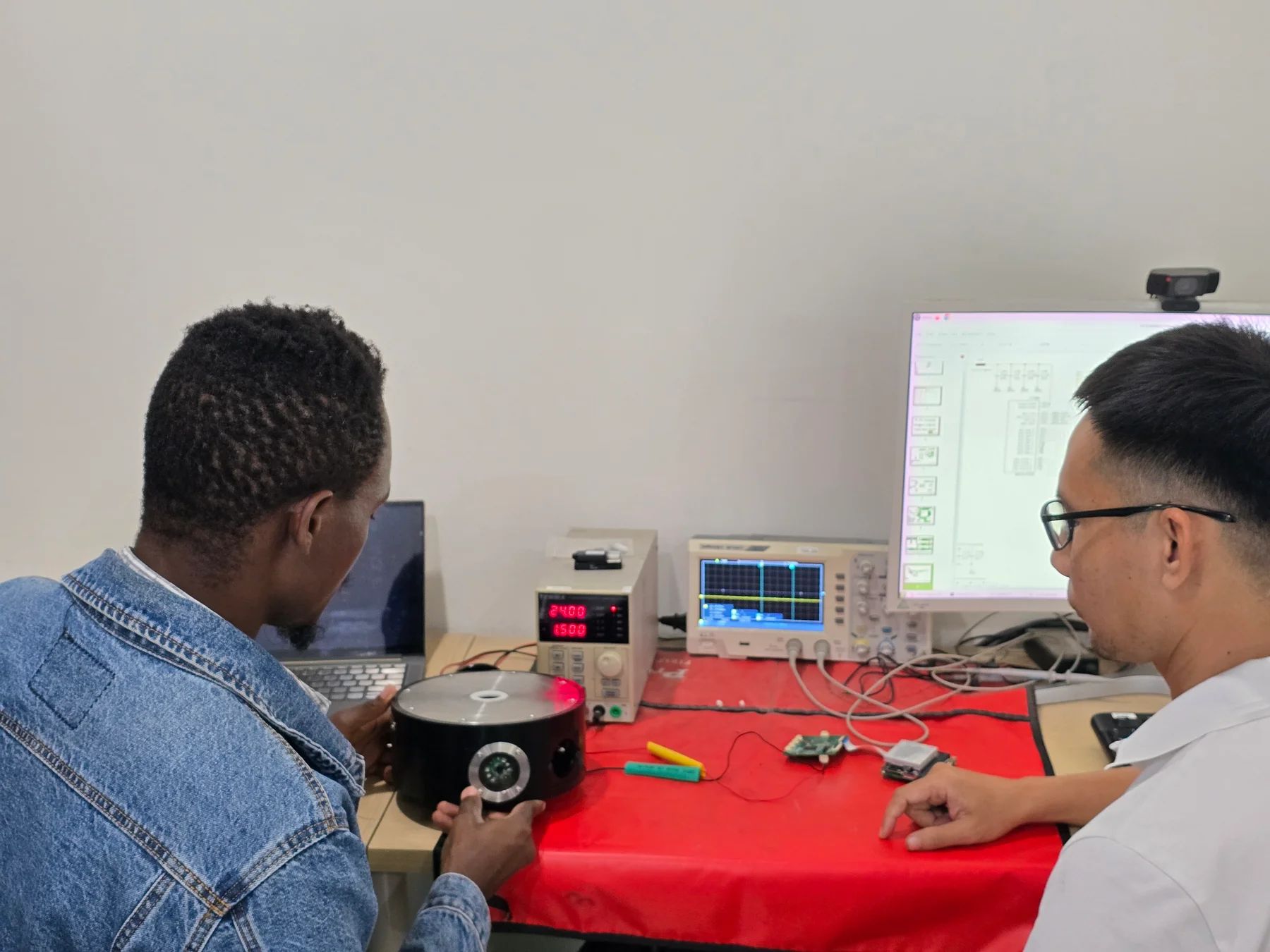 Two colleagues examining an instrument beside an oscilloscope, power supply and electronic components